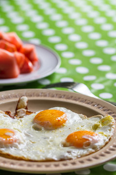 Fried eggs for breakfast with tomato in background