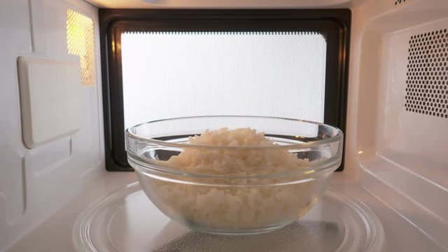 Glass bowl with cooked white rice reheating in the microwave oven inside view