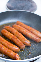 Frying homemade red sausages in frying pan
