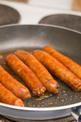 Frying homemade red sausages in frying pan