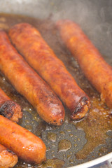 Frying homemade red sausages in frying pan