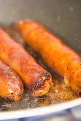 Frying homemade red sausages in frying pan