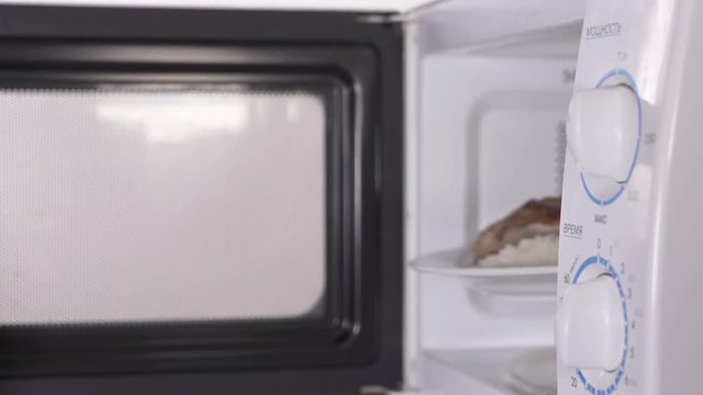 Personal chef who works in your microwave. Senior woman opens door of microwave to get food out man holds out his hand with a plate. Cooking concept 