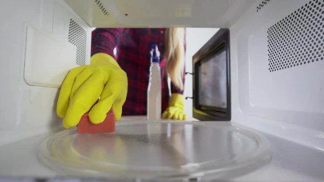 Cleaning microwave girl in protective gloves with sponge and cleaner wiping inside of the oven