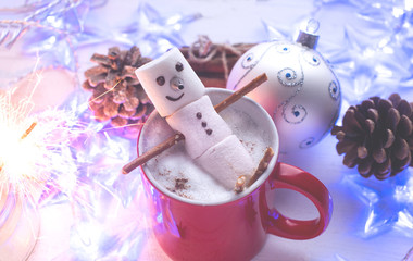 Funny marshmallow snowman in red cup of hot chocolate and sparklers