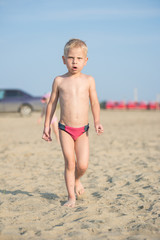 Baby boy walking on the sandy beach near the sea. Cute little kid at sand tropical beach. Ocean coast.