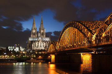 Fototapeta na wymiar Illuminated cologne cathedral and bridge after sunset with blue sky and dark clouds