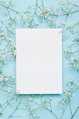 Wedding mockup with white paper list and flowers gypsophila on blue background from above....