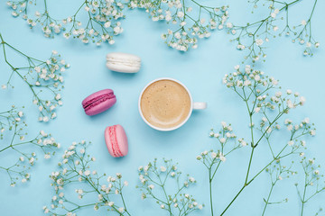 Morning cup of coffee, cake macaron and flower gypsophila on blue table from above. Cozy breakfast. Flat lay style.