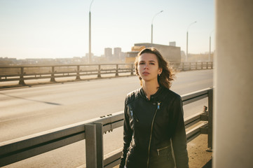 Obraz premium girl goes on road bridge. lonely young woman in black Leather jacket autumn, walking over the bridge which goes transport.