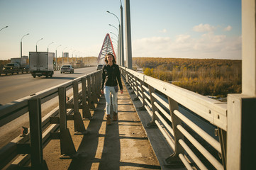 Fototapeta na wymiar girl goes on road bridge. lonely young woman in black Leather jacket autumn, walking over the bridge which goes transport.