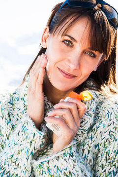 portrait d'une belle femme souriante se mettant de la cr&egrave;me de protection solaire en hiver