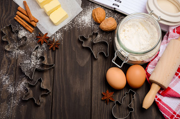 Christmas baking ingredients - cookies cutters, spices, butter, eggs and flour on dark wooden background, top view