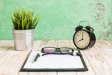 Wooden workplace desktop with clock; plants; glasses; Frame and pen.