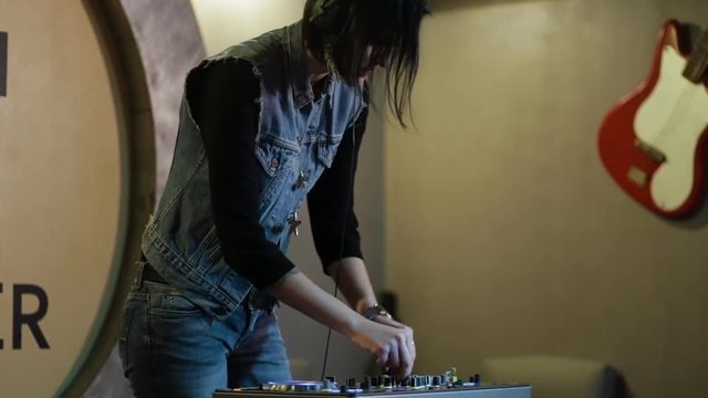 Woman DJ tweak different track controls on dj's deck at nightclub