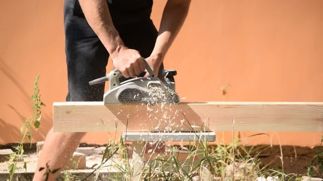 Hands of carpenter planes a beam with electric wood planer tool