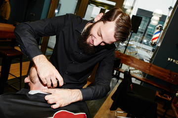 The Barber man in the process of cutting the beard of a client with an electric razor at the Barbershop