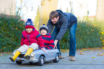 Two little kids boys and father playing with car, outdoors