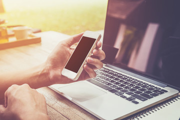 young business man hand holding phone and using laptop computer