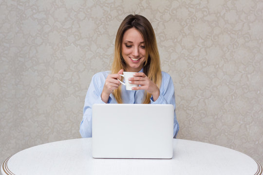 Young beautiful girl with a laptop at home at the table, smile,fun, cup of coffee or tea