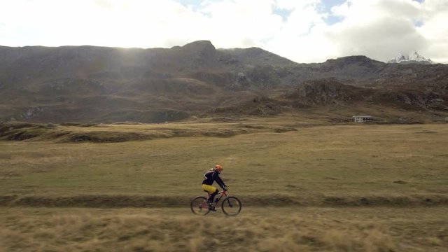 Aerial shot of mountain biker riding a grass covered trail on alpine pass in autumn season
