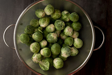 Fresh harvest of raw green Brussels sprouts in a metal colander on a brown wood background