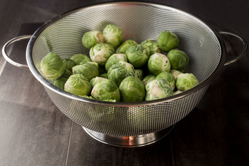 Fresh harvest of raw green Brussels sprouts in a metal colander on a brown wood background