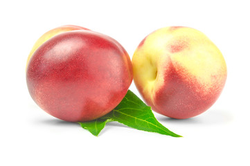 Two ripe nectarines with green leaves over white background