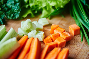 Vegetarian set of sliced carrots and cucumbers, garlic, green onion and lettuce on wooden Board closeup
