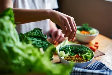 Female hand pours green onions in a bowl with green peas, cucumbers, carrots, lettuce and dill standing on a table © amixstudio