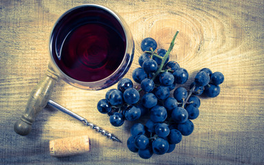 Glass of red wine with a sprig of grapes on a wooden table.
