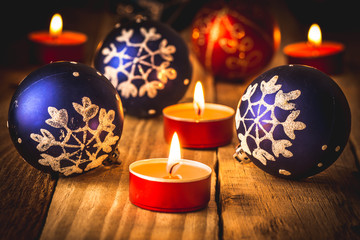 Blue and red Christmas balls and red lit candles on wood background