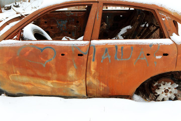 Strongly rusty skeleton of a burnt out car in the winter street