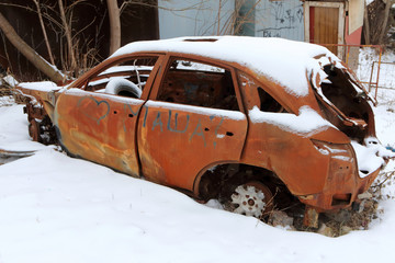 Strongly rusty skeleton of a burnt out car in the winter street