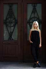 Obraz na płótnie Canvas Beautiful young blonde girl posing on the background of Burgundy doors. Sexy woman in a black dress. The girl on the background of the cityscape.