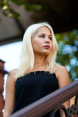 Young beautiful blonde girl posing on the background of the urban landscape. Sexy lady in a black dress with a pleasant appearance.