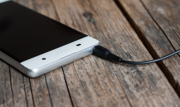 Klinkenstecker / Audiostecker, Smartphone wei&szlig; auf Holzuntergrund