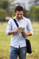 Young businessman is drinking coffee and using digital tablet at the park.