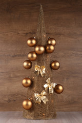 Decorative Christmas tree made from straw  with golden balls and bows isolated on wooden background