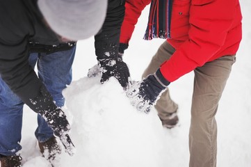 Guys rolled a big snowball to build a snowman in winter day
