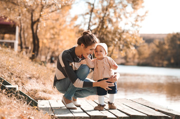 Smiling woman holding baby girl wearing knitted casual clothes outdoors.