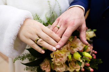 Bride and groom hands with wedding rings and flowers