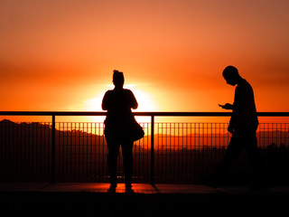 Man playing with cell phone instead of enjoying amazing deep orange sunset
