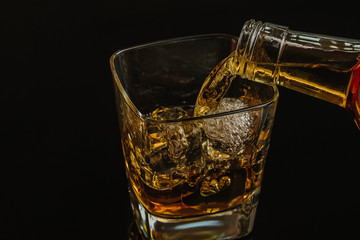 barman pouring whiskey with ice cubes in glass on black background, cool atmosphere