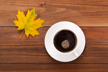 Cup of coffee and yellow maple leaf on a wooden background.