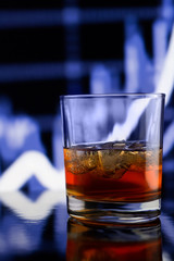 Whiskey glass with ice against blue blurred background
