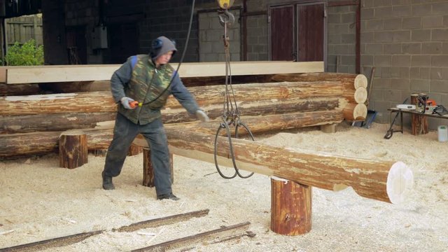 Builder raises wooden timber with Overhead Winch Crane. A man holds a log and transfer it to the future home