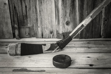 horizontal sepia image of an old vintage hockey stick with an old puck on a rustic old wood board background.