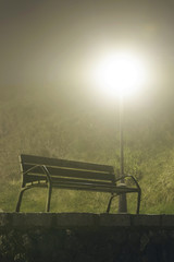 Mysterious park bench illuminated by a street light, on a foggy night.