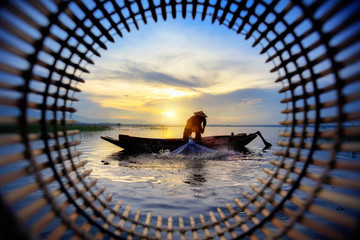 Silhouette fisherman throwing fishing net during sunrise